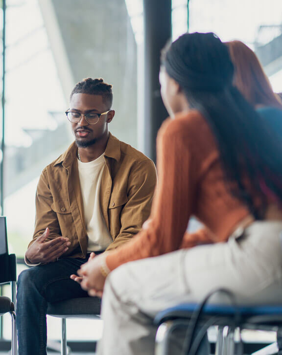 A small group of University students sit together during a group therapy session. They are each dressed casually as they take turns sharing their struggles with the group.