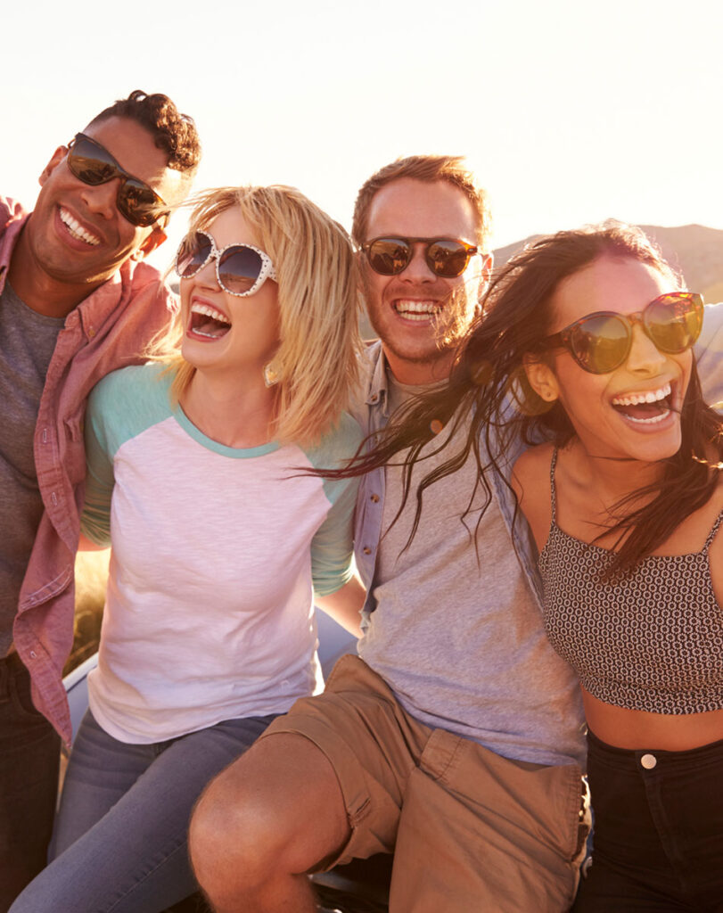 Friends On Road Trip Sitting On Hood Of Convertible Car