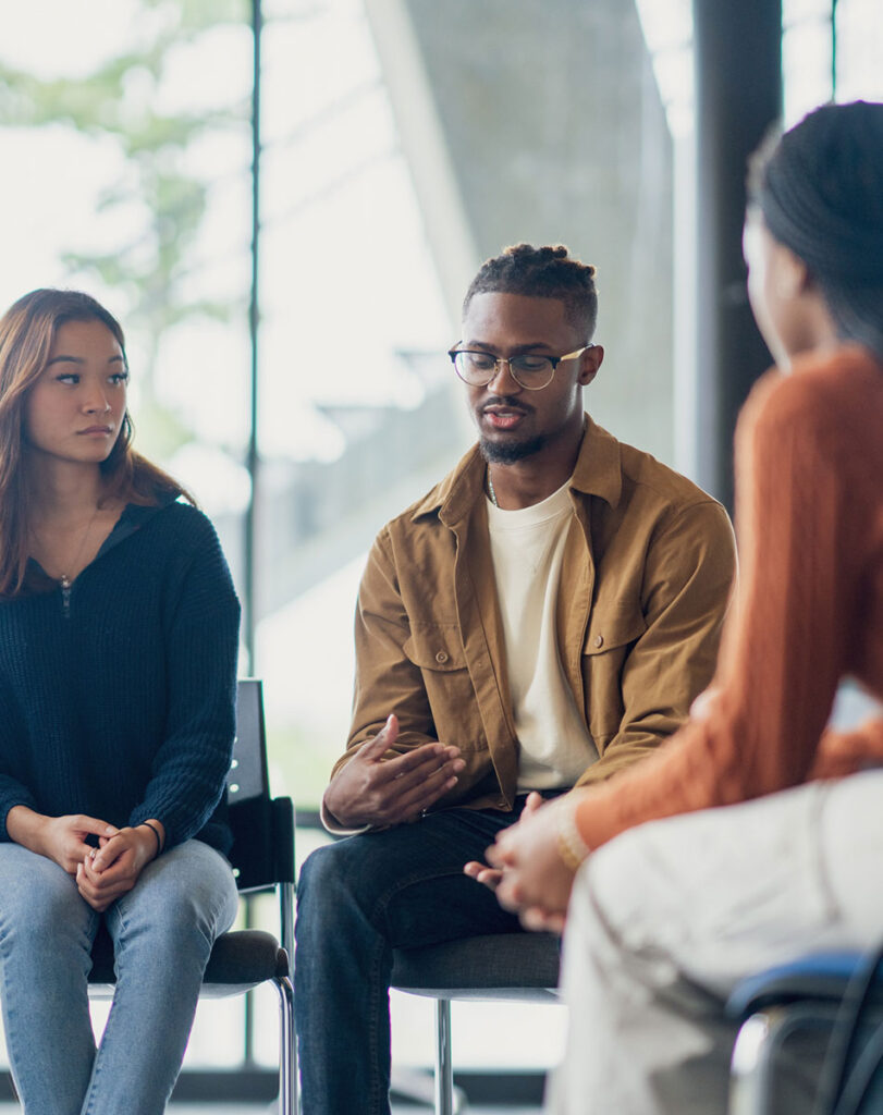 Multicultural group engaging in therapy session, expressing feelings and supporting each other.