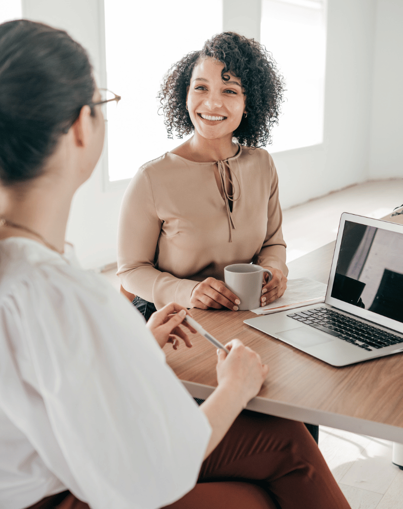 Two women in conversation at a table with a laptop